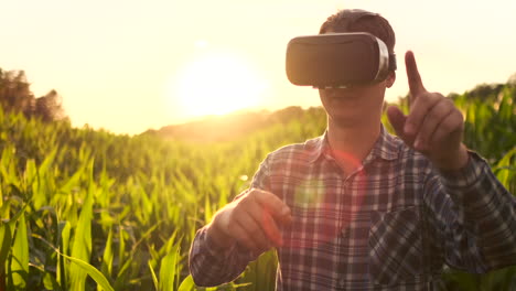 Ein-Männlicher-Bauer-Mit-Virtual-Reality-Brille,-Kariertem-Hemd-Und-Jeans-Steuert-Bei-Sonnenuntergang-Auf-Einem-Feld-Das-Maisbewässerungssystem.-Moderner-Landwirt,-Neue-Technologie,-Landwirt-Der-Zukunft